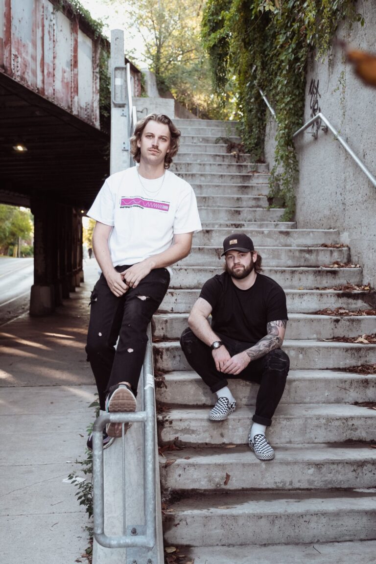 The DiscoGodFathers sitting on the stairs outside in a park by a railroad bridge