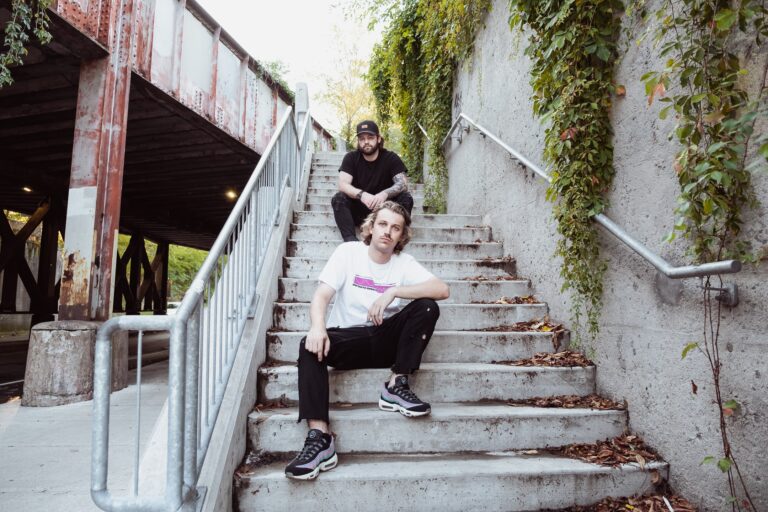 The DiscoGodFathers sitting on the stairs outside in a park by a railroad bridge